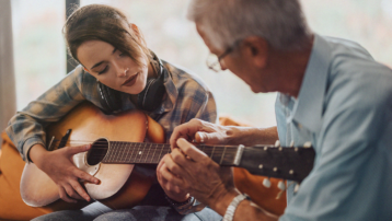 Volwassene leert onder begeleiding van een muziekdocent akoestische gitaar spelen