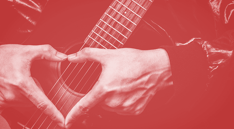 Een muzikant vormt een hart met zijn handen over een akoestische gitaar, als symbool van liefde voor muziek op Valentijnsdag.