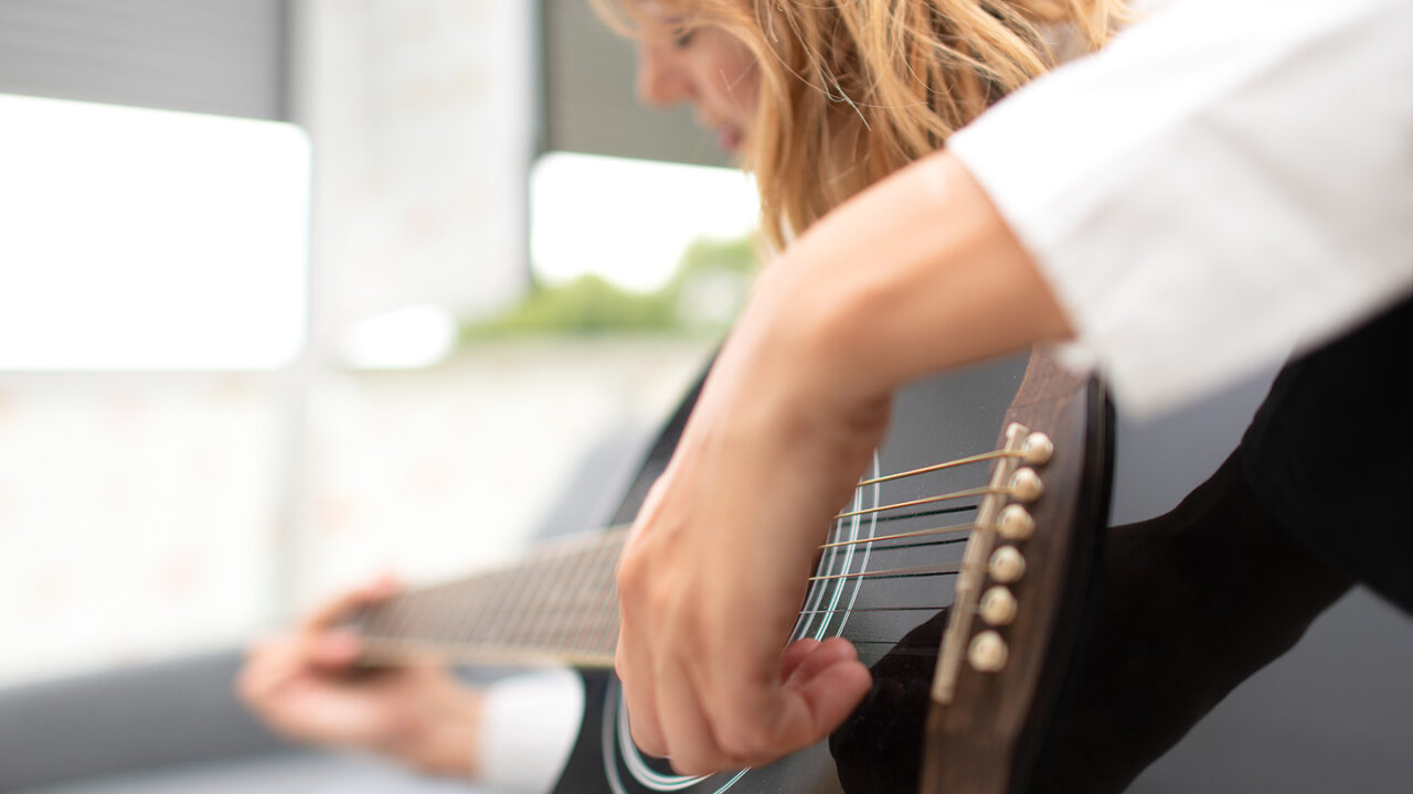 Close-up van een linkshandige muzikant die een zwarte akoestische gitaar aanslaat