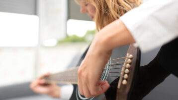 Close-up van een linkshandige muzikant die een zwarte akoestische gitaar aanslaat