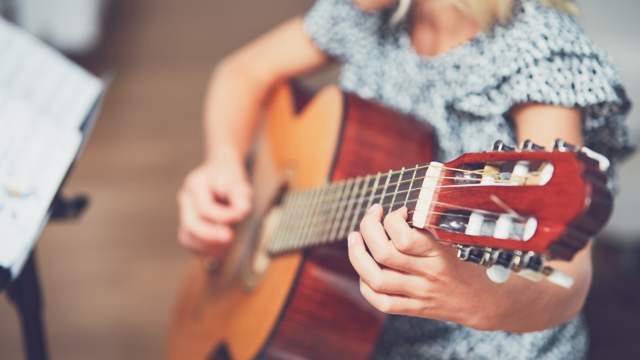 Kind dat op een kleine akoestische gitaar speelt en zo de juiste gitaarmaat voor kinderen illustreert.