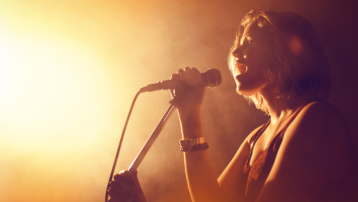 Zangeres zingt op het podium in een microfoon. De afbeelding illustreert 11 tips voor een krachtigere stem en een betere zangtechniek.