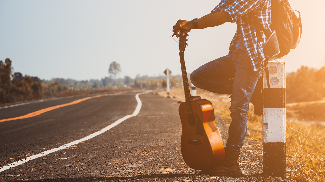 Muzikant met een reisgitaar langs een weg, klaar voor een vakantie en een muzikaal avontuur in de buitenlucht.