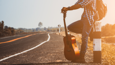 Muzikant met een reisgitaar langs een weg, klaar voor een vakantie en een muzikaal avontuur in de buitenlucht.