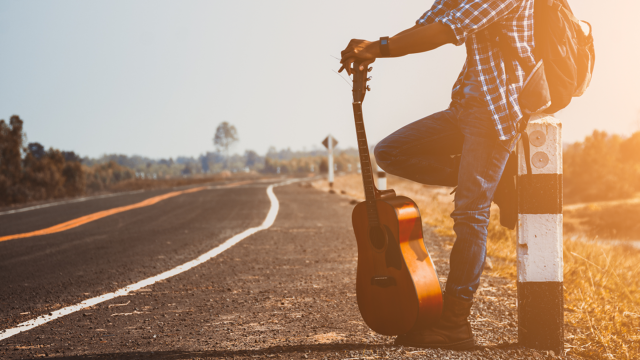 Muzikant met een reisgitaar langs een weg, klaar voor een vakantie en een muzikaal avontuur in de buitenlucht.