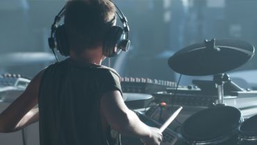 Jonge beginnende drummer draagt een hoofdtelefoon terwijl hij oefent op een elektronisch drumstel en de basis van het drummen onder de knie krijgt.