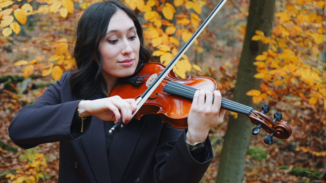 Een violist oefent buiten in de herfst en demonstreert een correcte strijkstokvoering en handhouding voor strijkinstrumenten.