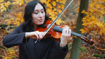 Een violist oefent buiten in de herfst en demonstreert een correcte strijkstokvoering en handhouding voor strijkinstrumenten.