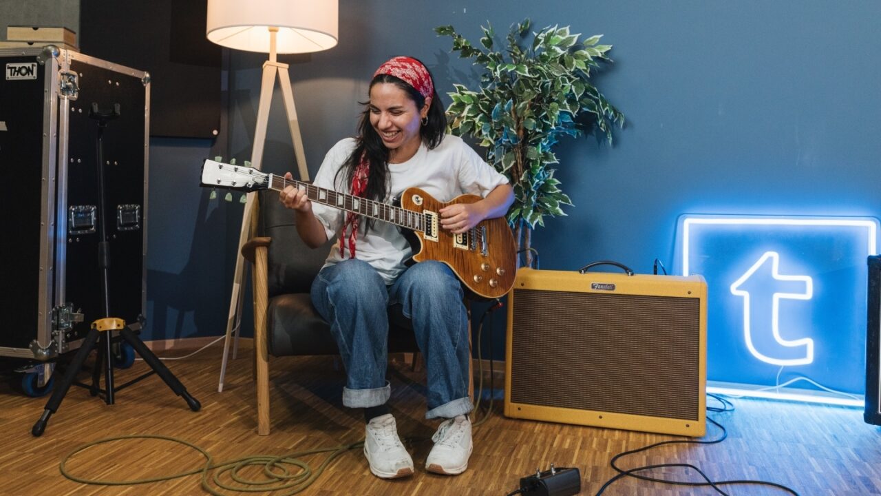 Beginner-gitarist lacht terwijl ze op een Les Paul elektrische gitaar speelt voor een Fender-versterker in een muziekkamer: Beginner-gitarist lacht terwijl ze op een Les Paul elektrische gitaar speelt voor een Fender-versterker in een muziekkamer: Beginnersgids voor Gitaarversterkers