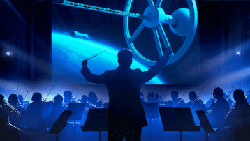 Dirigent en orkest voeren uit met een ruimtestation op de achtergrond, verwijzend naar de scène met An der schönen blauen Donau uit 2001: A Space Odyssey