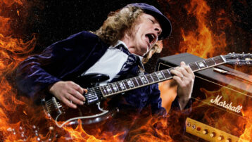 Angus Young van AC/DC in actie met zijn iconische Gibson SG, spelend voor een muur van vlammen en een Marshall-stack.