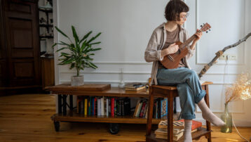 Persoon die binnenshuis ukelele speelt, als symbool voor de mentale en emotionele voordelen van het leren bespelen van een muziekinstrument