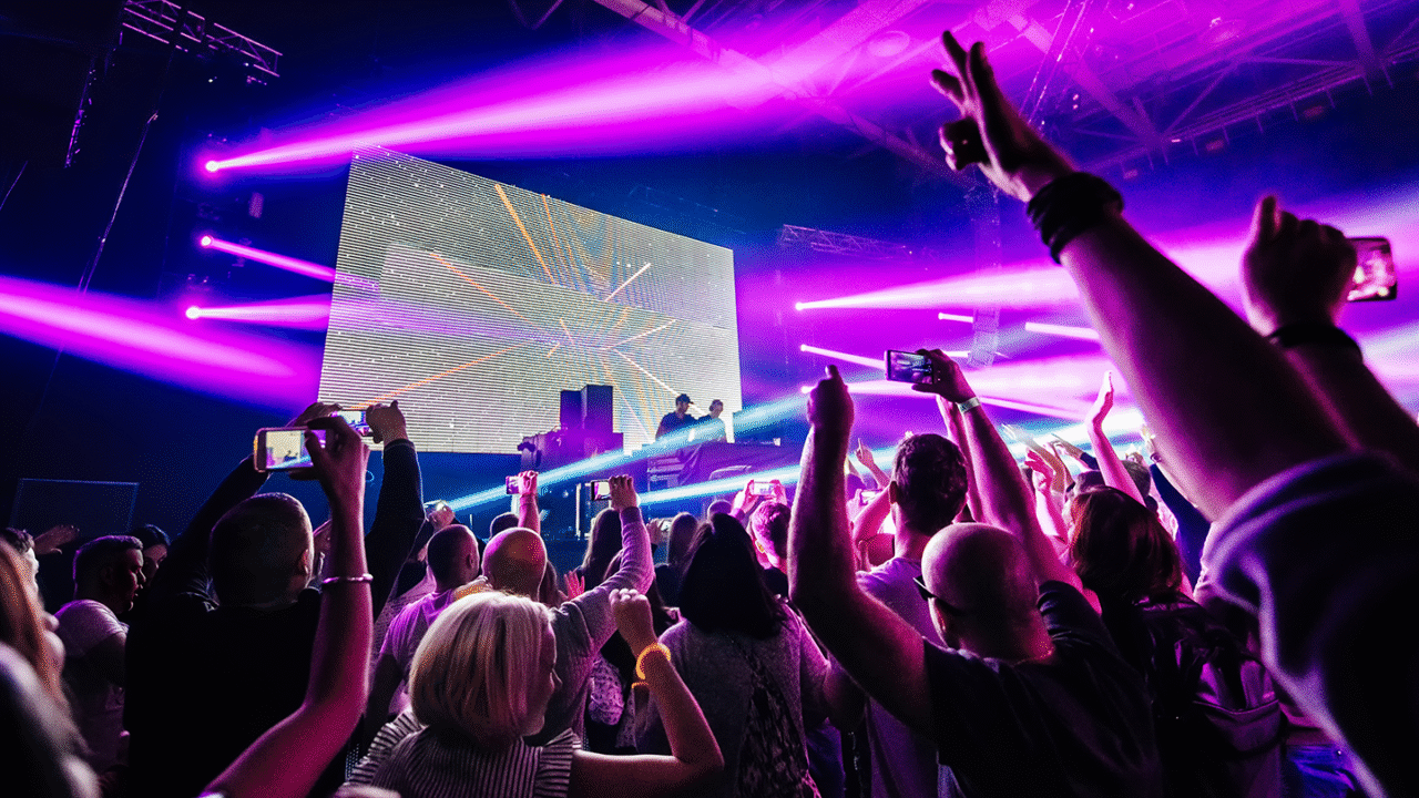 DJ die on-stage effects gebruikt tussen felroze en paarse verlichting, terwijl het publiek de handen in de lucht gooit.