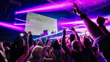 DJ die on-stage effects gebruikt tussen felroze en paarse verlichting, terwijl het publiek de handen in de lucht gooit.