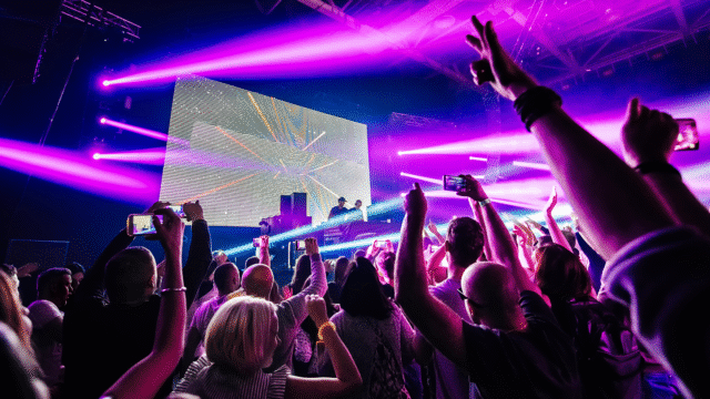 DJ die on-stage effects gebruikt tussen felroze en paarse verlichting, terwijl het publiek de handen in de lucht gooit.
