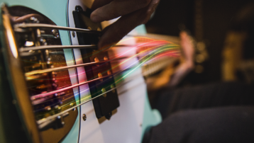 Close-up van een bassist die de snaren van een elektrische bas aanslaat, met kleurrijke lichtstrepen