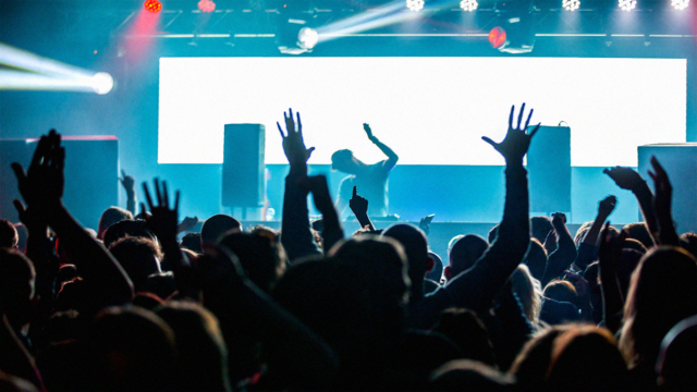 DJ die live draait in een club terwijl het publiek de handen omhoog steekt en reageert op een volle dansvloer