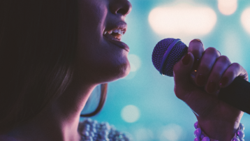 Close-up van een vrouw die op een podium in een microfoon zingt, als illustratie van de menselijke stem als uniek muzikaal instrument