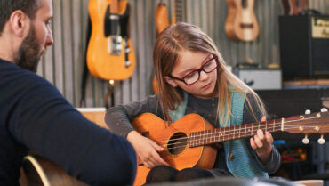 Kind leert akoestische gitaar spelen met een muziekdocent – zo kies je je eerste instrument