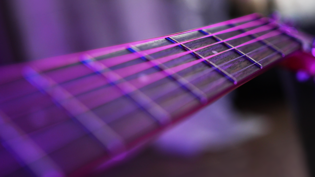 Close-up van de snaren en toets van een akoestische gitaar, verlicht met paars licht.